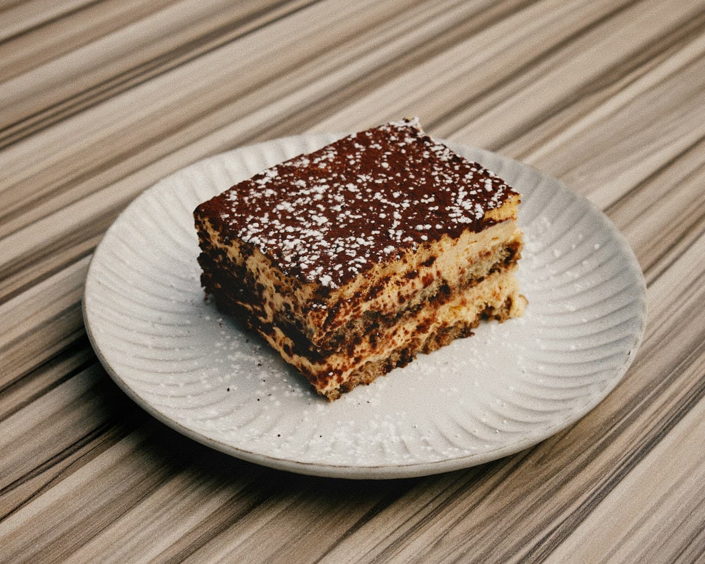 A square of classic layered Tiramisù dusted with cocoa